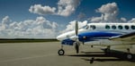 Un avion King Air A100 stationné de profil sur le tarmac par une journée d’été.