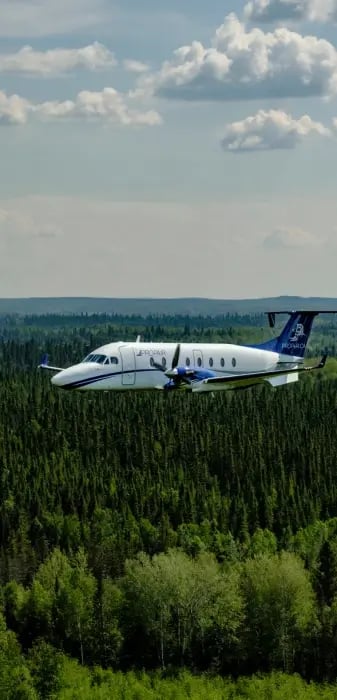 A Propair B1900D aircraft flying over a coniferous forest.