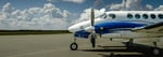 A King Air A100 aircraft parked on the tarmac on a summer day.