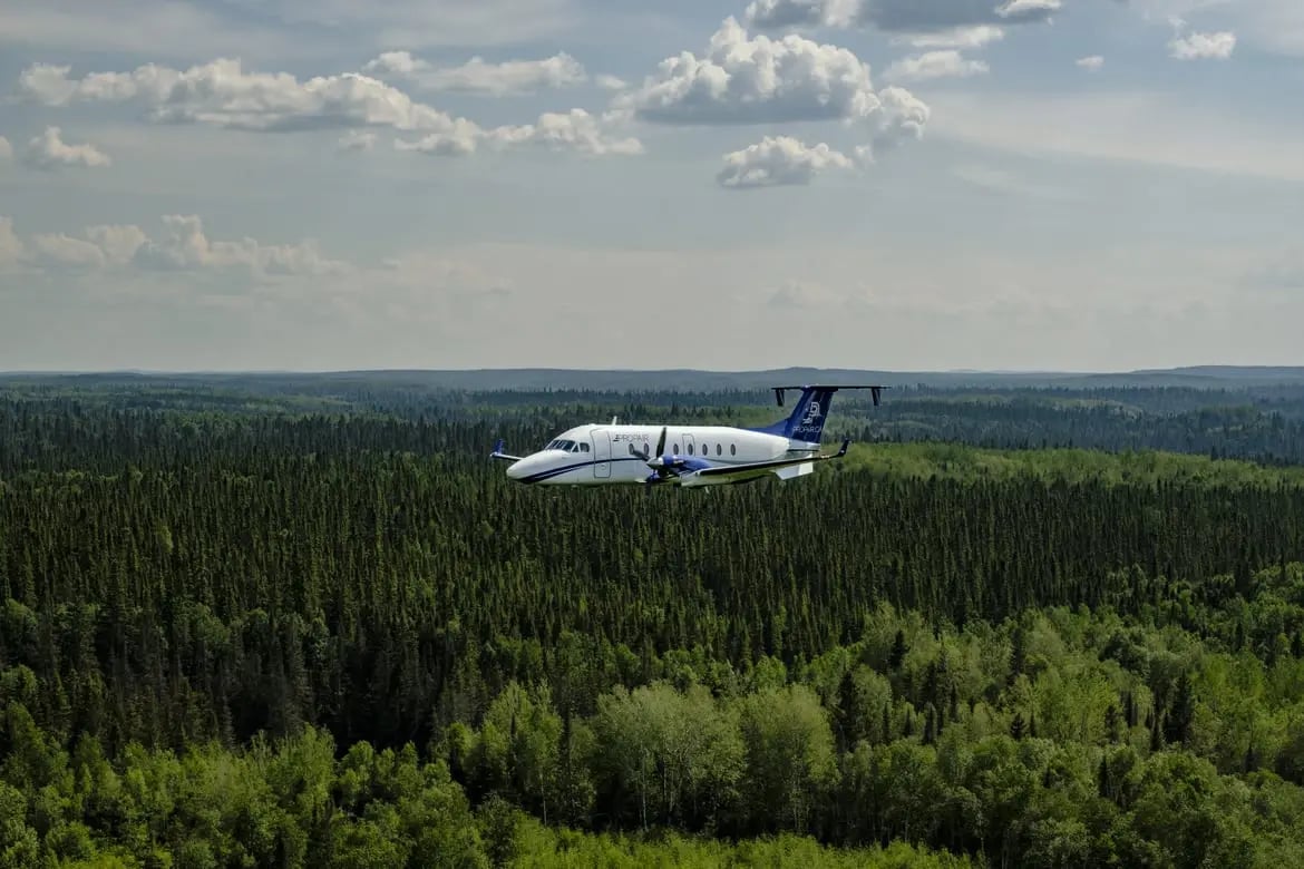 Un avion B1900D de Propair en vol au-dessus d’une vaste forêt de conifères.