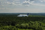 Un avion B1900D de Propair en vol au-dessus d’une vaste forêt de conifères.